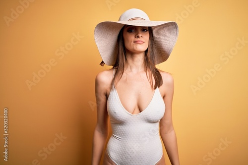 Young beautiful brunette woman on vacation wearing swimsuit and summer hat looking sleepy and tired, exhausted for fatigue and hangover, lazy eyes in the morning.
