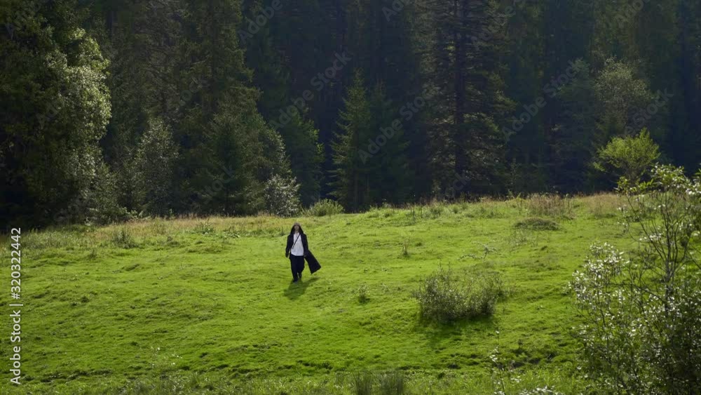 Wandering Missionary Medieval Monk Across Countryside. Man In Black Cloak Coat With Hood Walks On Rural Road In Mountain Forest. Slow Motion Wandering Missionary Medieval Monk Across Countryside. Man In Black Cloak Coat With Hood Walks On Rural Road In Mountain Forest. Slow Motion