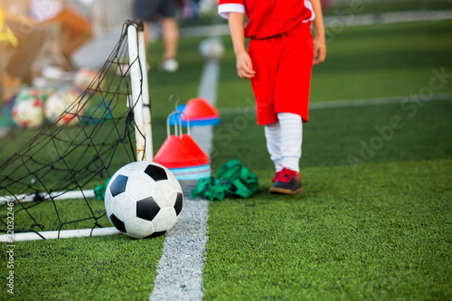 Soccer ball with blurry kid player and soccer training equipment on green artificial turf. Marker cones with exercise ladder drill and mini goal in soccer academy.