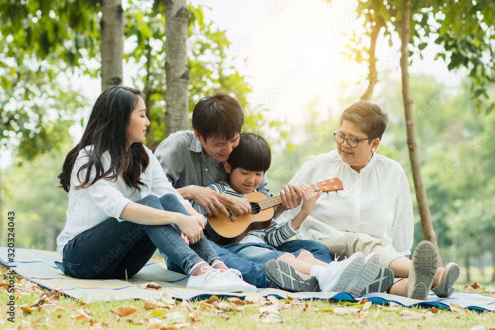 Happy family with grandma, mom with dad teaching son playing guitar and sing a song in park, Enjoy and relax people picnic outside Happy family with grandma, mom with dad teaching son playing guitar and sing a song in park, Enjoy and relax people picnic outside