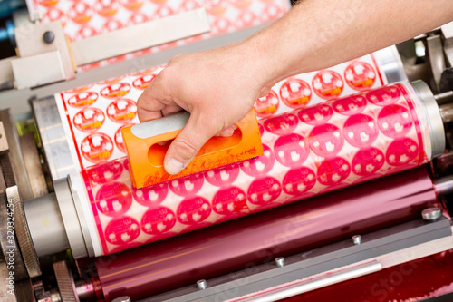 Process of removing possible dust debris on polymer plate in magenta print tower station with sticky roll on flexographic printing press. Dirt removing from photopolymer in flexo print machine.