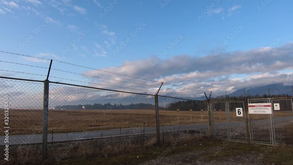 Time lapse moving clouds over Alps mountains and barb wire fence Ljubljana airport with sign security restricted area, Slovenia Time lapse moving clouds over Alps mountains and barb wire fence Ljubljana airport with sign security restricted area, Slovenia