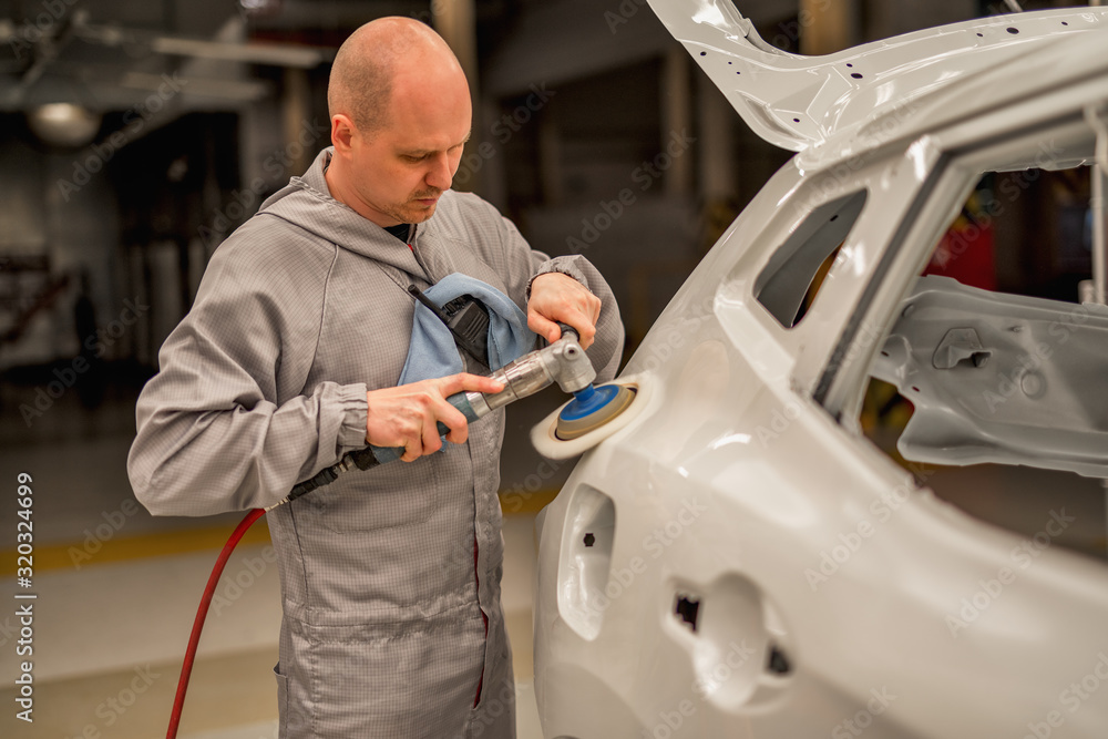 An employee in the paint shop of an automobile plant polishes painted body parts An employee in the paint shop of an automobile plant polishes painted body parts
