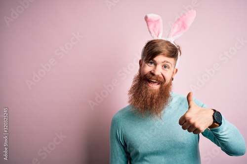 Canvas Print Hipster Irish man with beard wearing easter rabbit ears over isolated pink background doing happy thumbs up gesture with hand