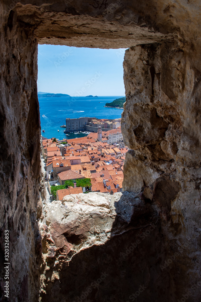 The UNESCO world heritage site Dubrovnik, Croatia, is framed against the Old City Walls. The Adriatic sea and terracotta roof tops and buildings are framed by a window.