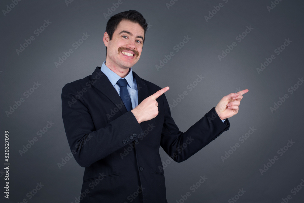 Pretty young man with positive expression, dressed casually, indicates with fore finger at blank copy space for your promotional text or advertisement. Adorable man poses indoor alone Pretty young man with positive expression, dressed casually, indicates with fore finger at blank copy space for your promotional text or advertisement. Adorable man poses indoor alone
