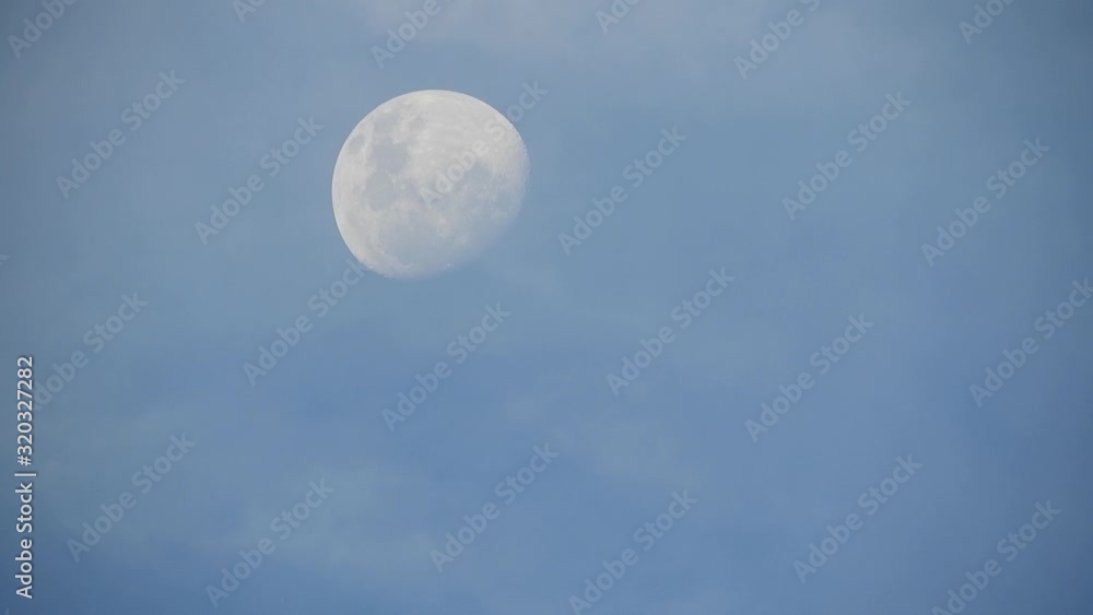 Twilight near full moon moving across the late afternoon sky before sunset with clouds moving past, clear visible crater detail Twilight near full moon moving across the late afternoon sky before sunset with clouds moving past, clear visible crater detail
