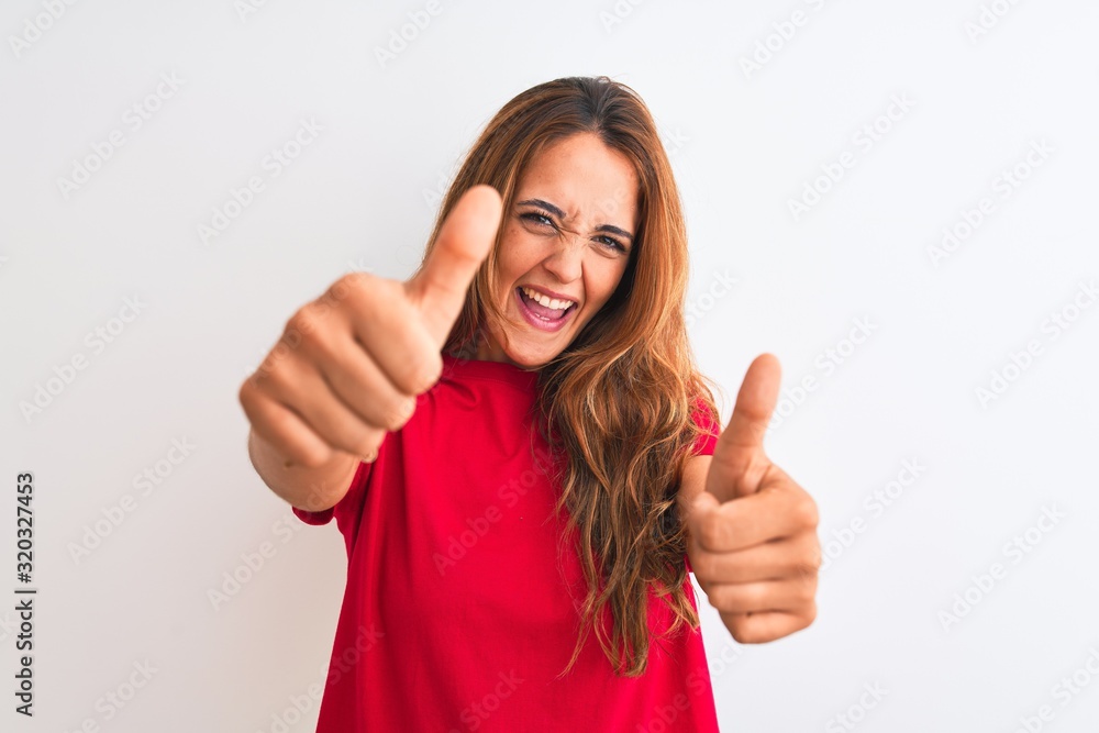 Young redhead woman wearing red casual t-shirt stading over white isolated background approving doing positive gesture with hand, thumbs up smiling and happy for success. Winner gesture. Young redhead woman wearing red casual t-shirt stading over white isolated background approving doing positive gesture with hand, thumbs up smiling and happy for success. Winner gesture.