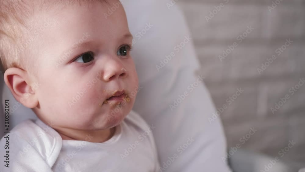 A baby is being fed by it’s mother with a spoon. The newborn is having a meal with food remains on it’s mouth. A baby is being fed by it’s mother with a spoon. The newborn is having a meal with food remains on it’s mouth.