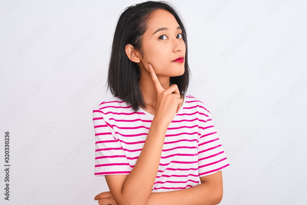 Young chinese woman wearing striped t-shirt standing over isolated white background with hand on chin thinking about question, pensive expression. Smiling with thoughtful face. Doubt concept. Young chinese woman wearing striped t-shirt standing over isolated white background with hand on chin thinking about question, pensive expression. Smiling with thoughtful face. Doubt concept.