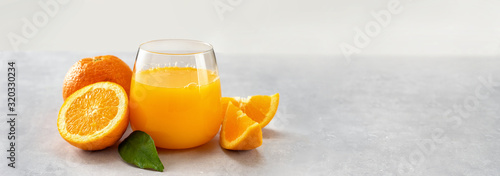 Fotografiet Fresh orange juice glass and oranges on light background