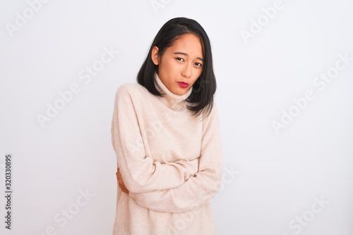 Young chinese woman wearing turtleneck sweater standing over isolated white background shaking and freezing for winter cold with sad and shock expression on face © Krakenimages.com