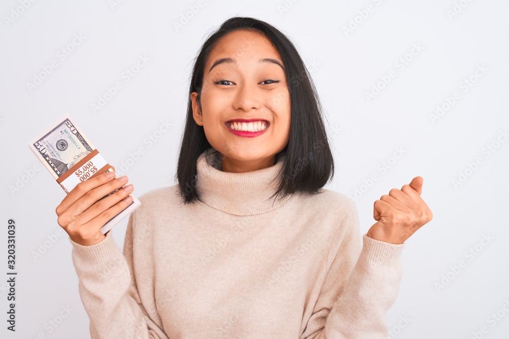 Young beautiful chinese woman holding dollars standing over isolated white background screaming proud and celebrating victory and success very excited, cheering emotion Young beautiful chinese woman holding dollars standing over isolated white background screaming proud and celebrating victory and success very excited, cheering emotion
