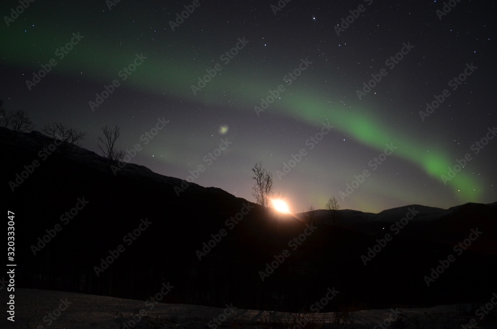 Aurora borealis pierce the night sky and the moon is rising up behind the mountain