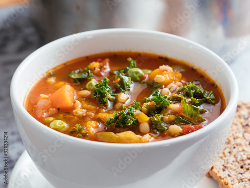 Home made Italian winter minestrone soup with winter squash, carrots, kale, green beans, peas, tomatoes and barley