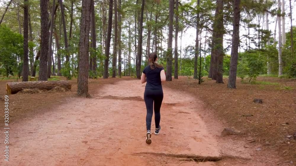 Girl jogging on a dirt trail between trees, camera follow her thtough the trail. Girl jogging on a dirt trail between trees, camera follow her thtough the trail.