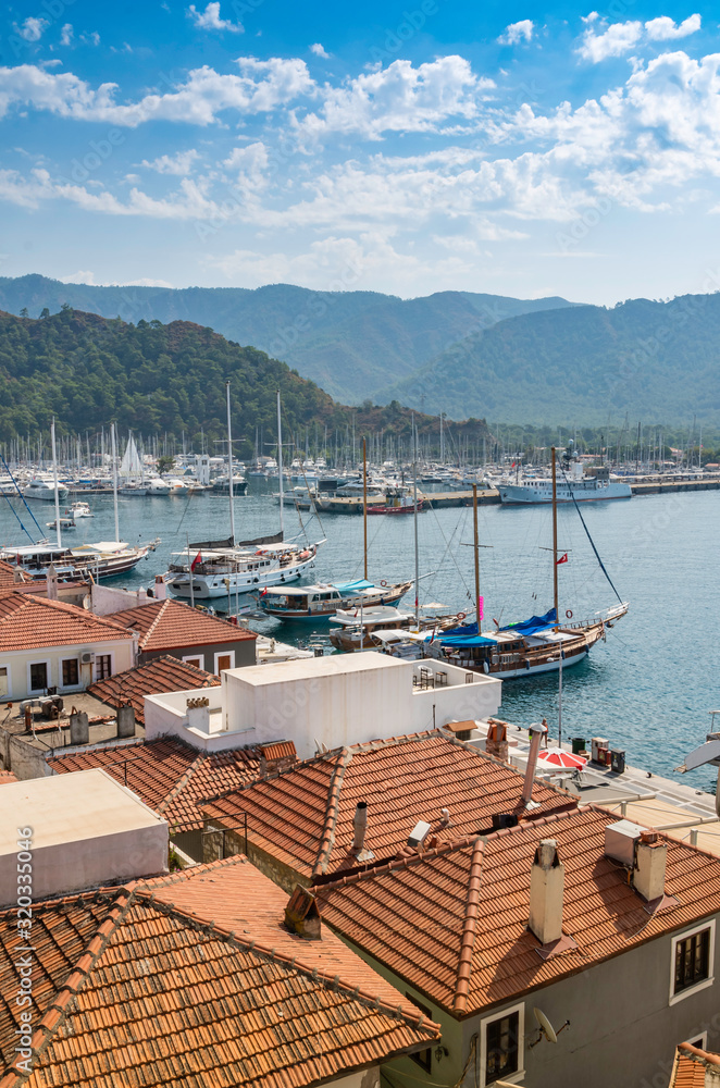 Marmaris Bay with yachts, tiled terracotta roofs of houses against the background of green mountains.