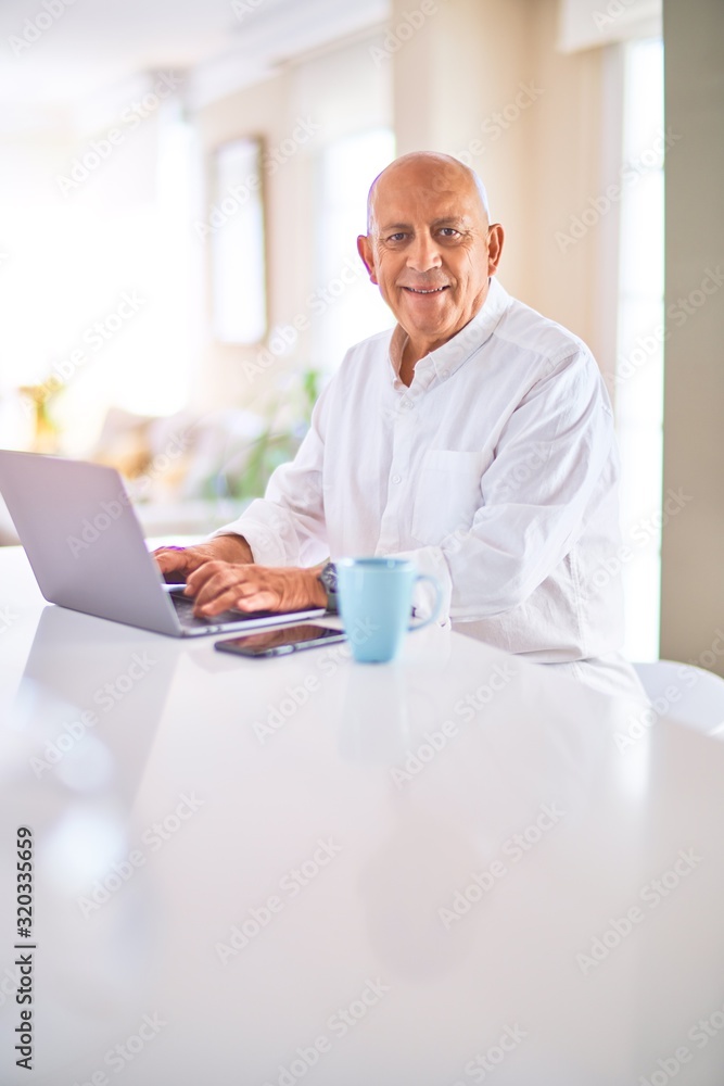 Senior handsome man smiling happy and confident. Sitting using laptop and drinking cup of coffee at home Senior handsome man smiling happy and confident. Sitting using laptop and drinking cup of coffee at home