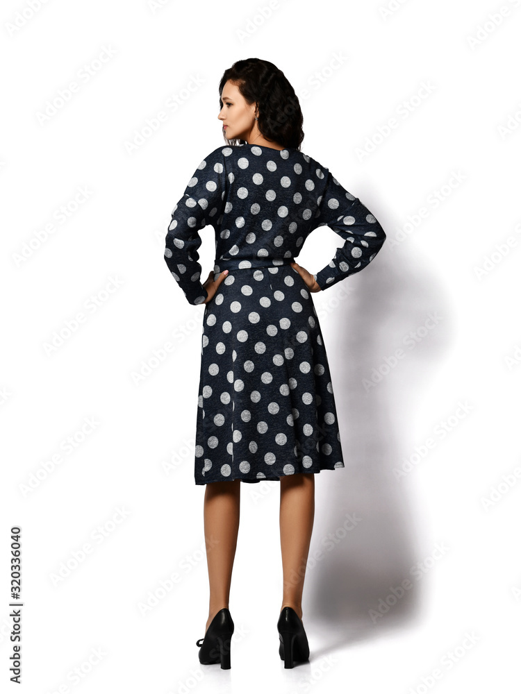 Young beautiful brunette curly smiling woman model in stylish vintage dark dotted midi dress and shoes standing backwards Young beautiful brunette curly smiling woman model in stylish vintage dark dotted midi dress and shoes standing backwards