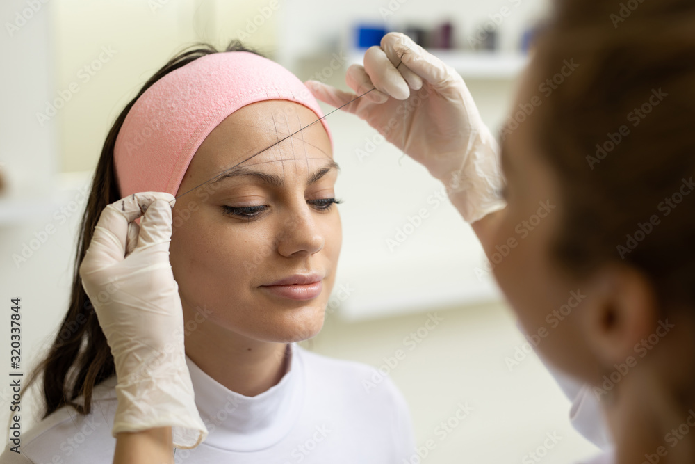 The girl beautician marks with the help of thread eyebrow tattoo. Permanent makeup. Permanent tattooing of eyebrows. The girl beautician marks with the help of thread eyebrow tattoo. Permanent makeup. Permanent tattooing of eyebrows.