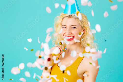 Portrait of a happy  smiling young woman celebrating fun birthday party amid confetti falling  isolated on blue
