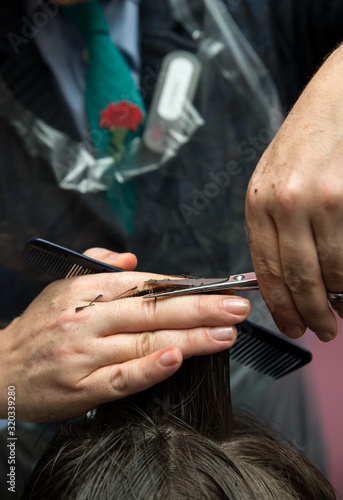 Hands of professional hair stylist cutting client shot hair.