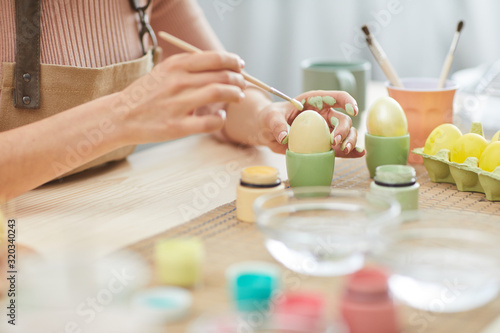 Close up of unrecognizable young woman painting eggs in pastel colors for Easter while sitting at table in kitchen or art studio  copy space