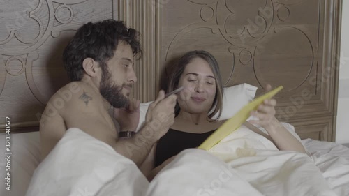 An attractive girl in bed forcing a guy to sign an agreement before having sex