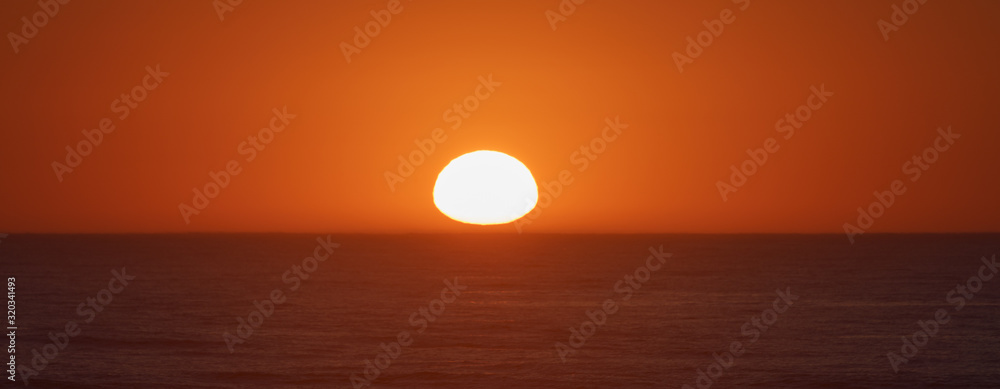 Breathtaking hot red sunset over the Atlantic ocean. Sun disc hanging over the horizon line. The ocean is calm and peaceful during this magic sunny summer sunset time in French Nouvelle-Aquitaine 