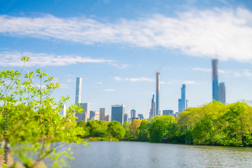 Midtown Manhattan skyscraper stand beyond the many growing fresh green trees along The Lake in Central Park in Central Park New York City NY USA on May. 08 2019.
