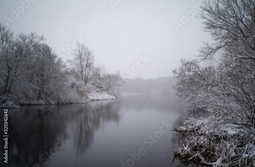 A Snowy Scene Of A Pond Surrounded By Trees