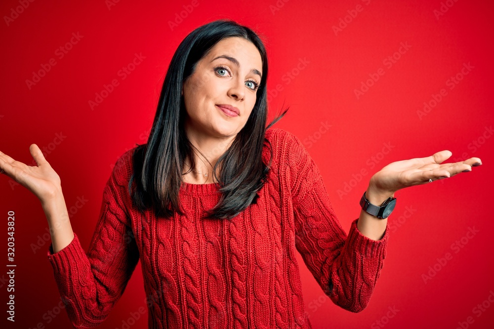 Young brunette woman with blue eyes wearing casual sweater over isolated red background clueless and confused expression with arms and hands raised. Doubt concept. Young brunette woman with blue eyes wearing casual sweater over isolated red background clueless and confused expression with arms and hands raised. Doubt concept.