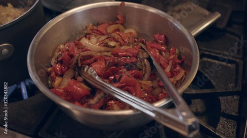 bowl of fresh grilled red peppers and onions on stove top with tongs close up photo