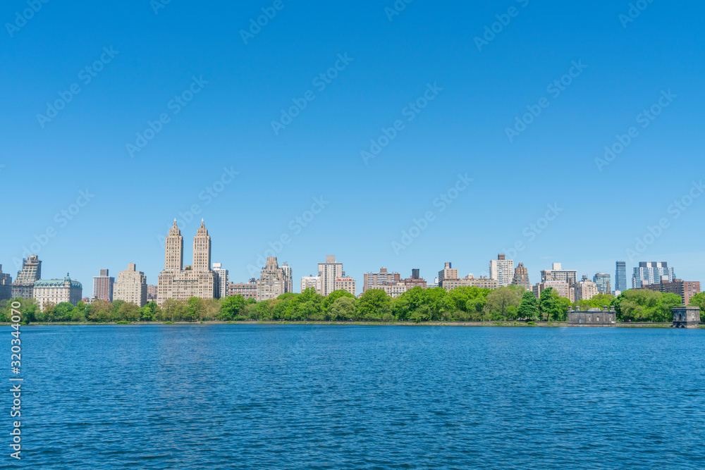 Central Park West Historical District Buildings stand beyond the Central Park Reservoir along the row of growing fresh green trees in Central Park New York City NY USA on May. 11 2019.