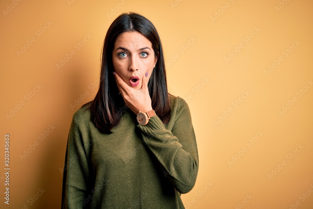Young brunette woman with blue eyes wearing green casual sweater over yellow background Looking fascinated with disbelief, surprise and amazed expression with hands on chin Young brunette woman with blue eyes wearing green casual sweater over yellow background Looking fascinated with disbelief, surprise and amazed expression with hands on chin
