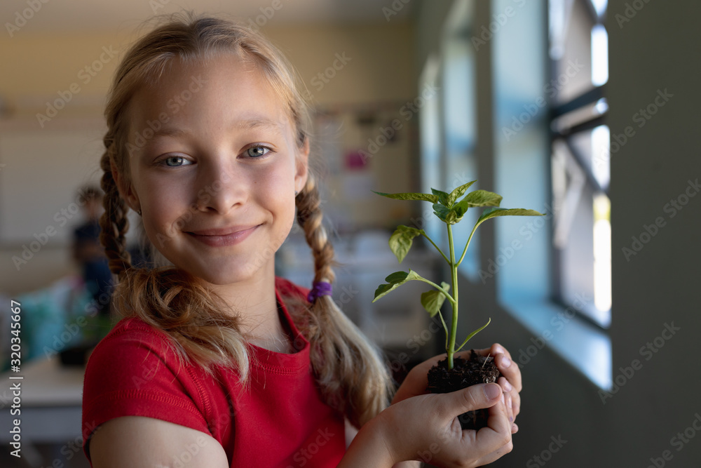 Schoolgirl standing holding a seedling plant in earth in an elementary school classroom Schoolgirl standing holding a seedling plant in earth in an elementary school classroom