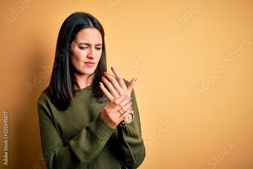 Obraz na plátne Young brunette woman with blue eyes wearing green casual sweater over yellow bac