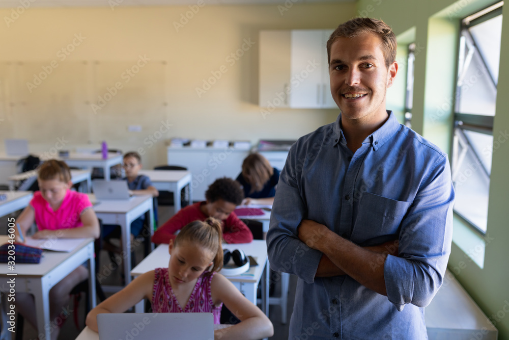 Fototapeta premium Male school teacher standing with arms crossed in an elementary school classroom