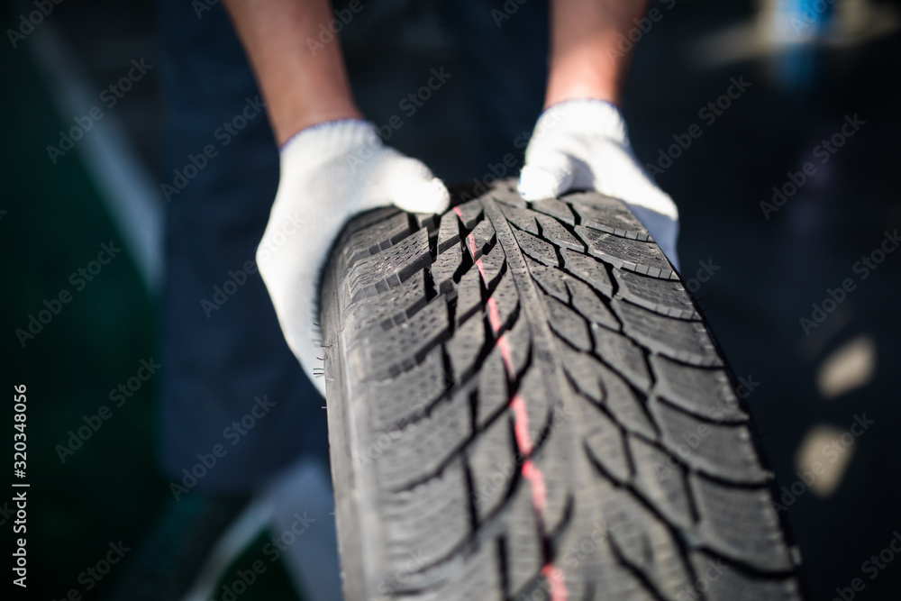 Closeup of man mechanic hands pushing a black tire in the workshop.