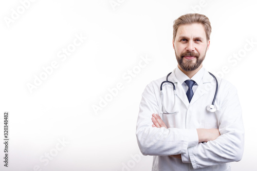 Smiling bearded doctor in white coat with stethoscope posing arms crossed isolated white background copyspace