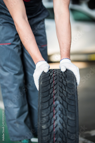 Close up of man mechanic carrying a tire in tire service.
