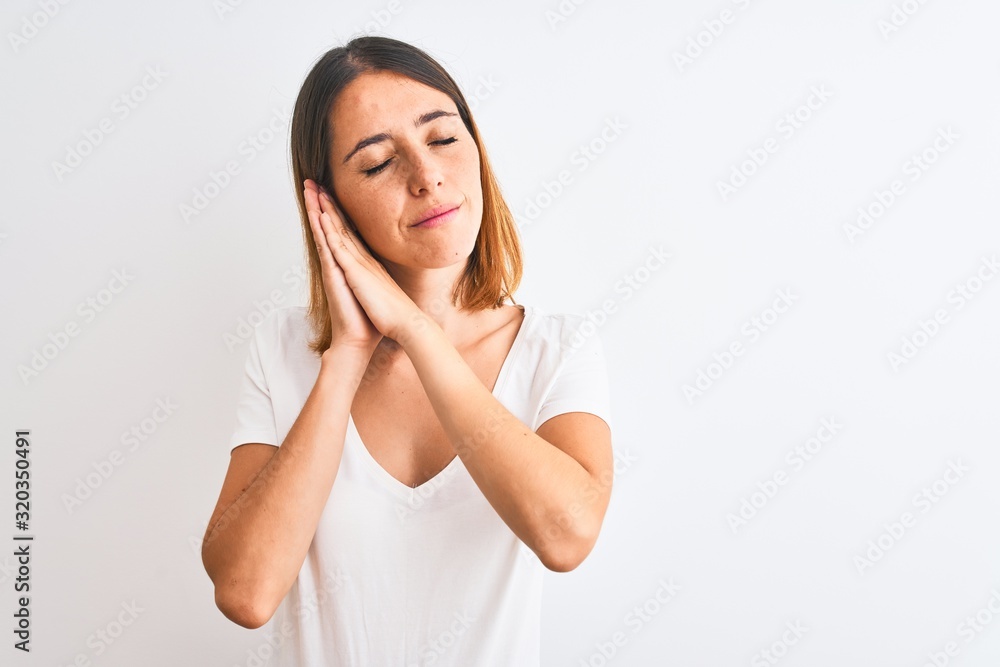 Beautiful redhead woman wearing casual white t-shirt over isolated background sleeping tired dreaming and posing with hands together while smiling with closed eyes. Beautiful redhead woman wearing casual white t-shirt over isolated background sleeping tired dreaming and posing with hands together while smiling with closed eyes.
