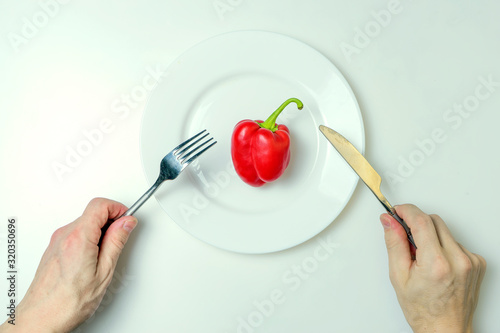 Diet concept. Men's hands hold a fork and knife over a plate with red pepper.