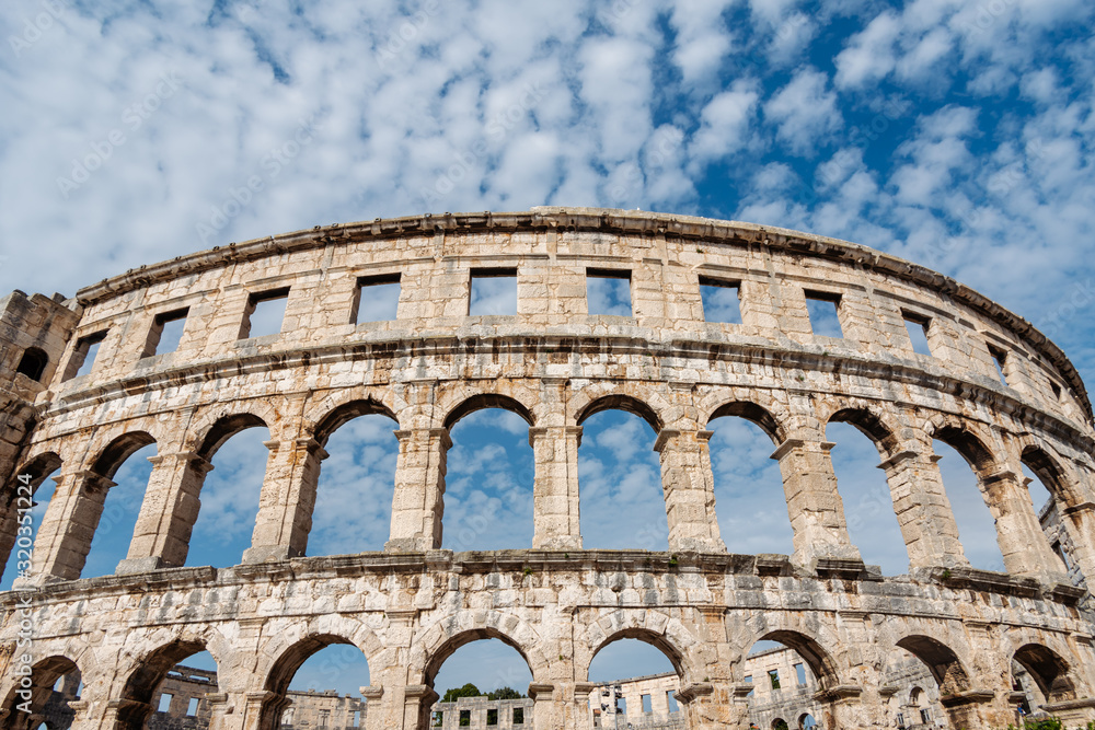 Exterior facade of the historic Roman Empire gladiator amphitheatre Coliseum and blue sky with beautiful white clouds on the background, Pula, Croatia. 