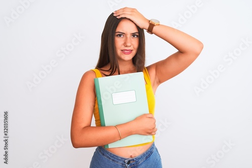 Young beautiful student girl holding notebook standing over isolated white background stressed with hand on head, shocked with shame and surprise face, angry and frustrated. Fear and upset