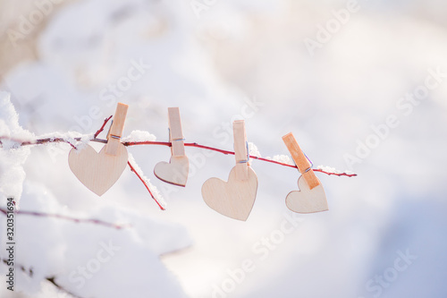 a garland of wooden hearts hangs on a snow-covered branch. The concept of Valentine's Day .
