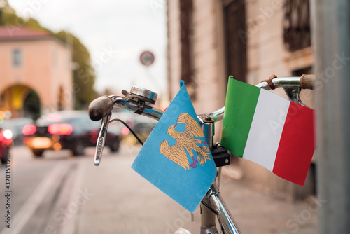 Small Italian flag and Fiuli's flags on a parked bicycle in Piazza Primo Maggio, Udine. National/regional celebrations on unity.