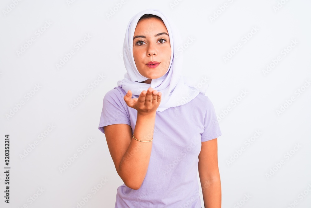 Young beautiful arabian girl wearing hijab standing over isolated white background looking at the camera blowing a kiss with hand on air being lovely and sexy. Love expression. Young beautiful arabian girl wearing hijab standing over isolated white background looking at the camera blowing a kiss with hand on air being lovely and sexy. Love expression.