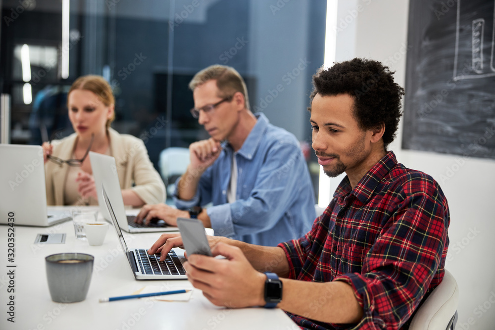 Fototapeta premium Afro american guy using cellphone while working with colleagues