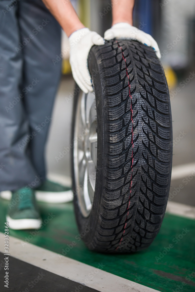 Auto mechanic carrying tire in tire store Auto mechanic carrying tire in tire store
